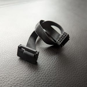 以下が含まれることがあります： 2つのコネクタが付いた黒いリボンケーブル。1つのコネクタはピンが並んだもので、もう1つはバネ式のラッチです。