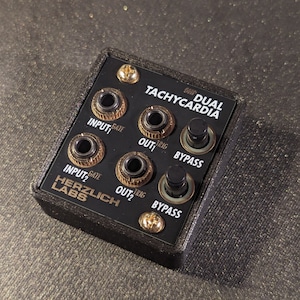 May include: A black and gold dual TACHYCARDIA effects pedal with two input jacks, two output jacks, and two bypass switches. The pedal is labeled "HERZLICH LABS".