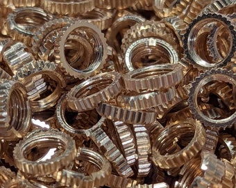 May include: A close-up shot of a pile of small, gold-colored metal rings. Each ring has a ridged outer edge and a threaded inner diameter. The rings are densely packed together, creating a textured surface.