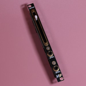 Può includere: Modulo elettronico nero e oro con il testo "OFFSET" e "OFFSET 1" e "OFFSET 2" e un simbolo di cuore. Il modulo ha uno slider bianco e tre jack neri.
