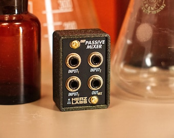 May include: A black and gold passive mixer with four input jacks and one output jack. The text "OHP PASSIVE MIXER" is printed above the jacks, and the Herz Labs logo is at the bottom. The mixer is rectangular and has a textured finish.