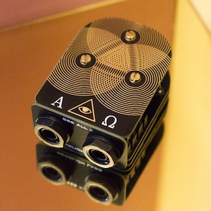 May include: A black and gold electronic device with a circular pattern and three knobs. The device has two black connectors on the bottom and the text "A Δ Ω SEE ALL II" on the front.