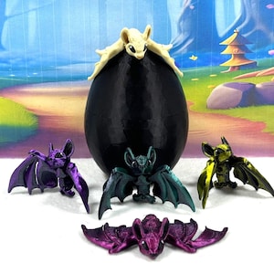 May include: Five small bat figurines, one with a green and black iridescent finish, one with a purple iridescent finish, one with a gold finish, and two with a purple finish. The bats are arranged around a black egg-shaped object with a white bat figurine on top.