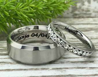 May include: Two silver wedding bands. The wider band has the inscription "Tanja 04/04" and the thinner band has a row of small clear stones and the inscription "Megumi".