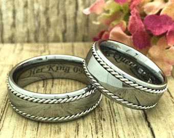 May include: Two silver wedding bands with a rope design around the edge. The band on the left has the inscription "Her King 09". The band on the right has the inscription "His Queen".
