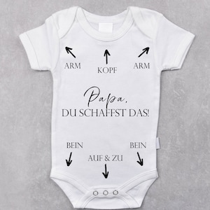 May include: White baby onesie with black text that reads "Papa. DU SCHAFFST DAS!" with arrows pointing to the head, arms, and legs.