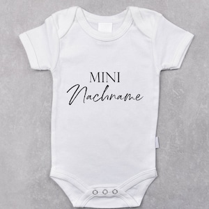Puede incluir: Un body blanco para bebé con texto negro que dice "MINI Nachname".