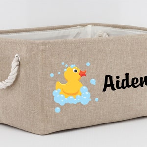 May include: A beige canvas storage bin with rope handles. The bin has a yellow rubber ducky with blue bubbles and the name "Aiden" printed on it.