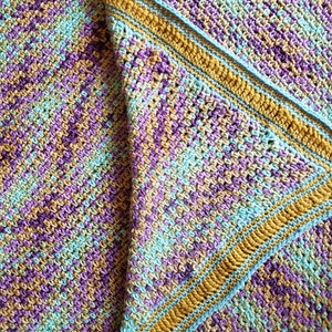 May include: A crocheted blanket with a multi-colored pattern in shades of purple, teal, and gold. The blanket has a border in teal and gold.
