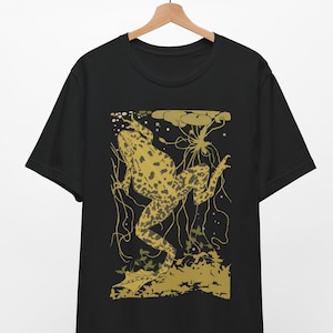 May include: A black short-sleeve t-shirt featuring a gold and dark green graphic print of a spotted frog swimming among aquatic plants and lily pads. The design is centered on the chest area, showcasing a detailed illustration of the amphibian.