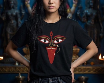 May include: Black t-shirt featuring a graphic of a deity's face with red, gold, and white details. The design includes large eyes, a nose ring, and a protruding tongue. The person is wearing dark blue jeans.