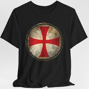 May include: Black t-shirt with a red cross in a circle on the front. The cross is on a white background with a distressed, vintage look.