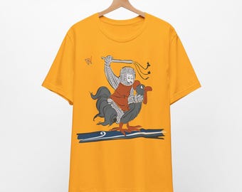 Puede incluir: Una camiseta amarilla de manga corta con un estampado gráfico de un caballero con armadura plateada montado sobre un gran gallo gris oscuro. El caballero sostiene un látigo sobre su cabeza, incluyendo un pequeño símbolo y una línea azul.