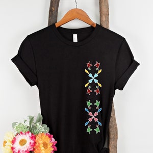以下が含まれることがあります： 前面にカラフルな幾何学模様が施された黒いTシャツ。デザインは、赤、黄、青、緑の4つのスタイリッシュな花で構成されています。