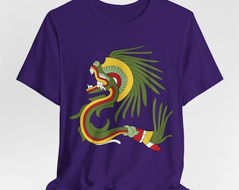 Puede incluir: Una camiseta de manga corta de color morado oscuro con un gráfico central de una serpiente estilizada en verde, amarillo y rojo con una cresta de plumas. La criatura aparece de perfil con la boca abierta, dientes afilados y plumas largas.