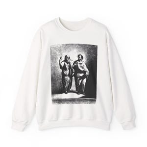 Może przedstawiać: Biała bluza z okrągłym dekoltem z czarno-białym nadrukiem dwóch postaci w szatach. Jedna postać podnosi ramię, druga wskazuje. Bluza jest w jednolitym białym kolorze.