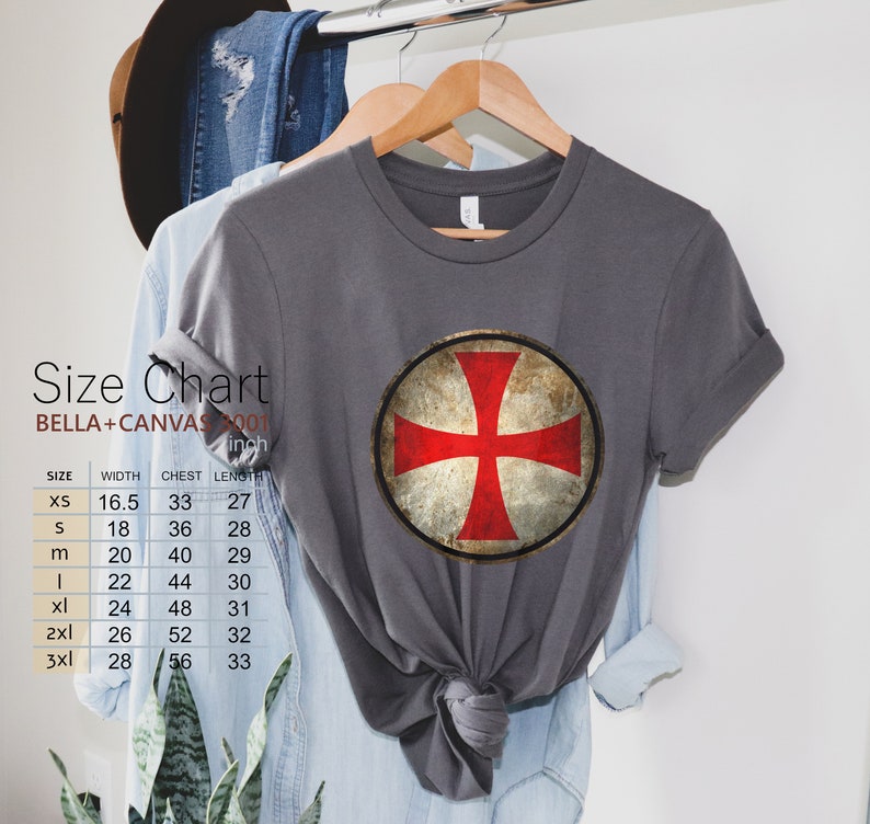 May include: A gray t-shirt with a red cross on a shield design. The shirt is a Bella + Canvas 2001 unisex t-shirt. The size chart shows the width, chest, and length in inches for sizes XS to 3XL.