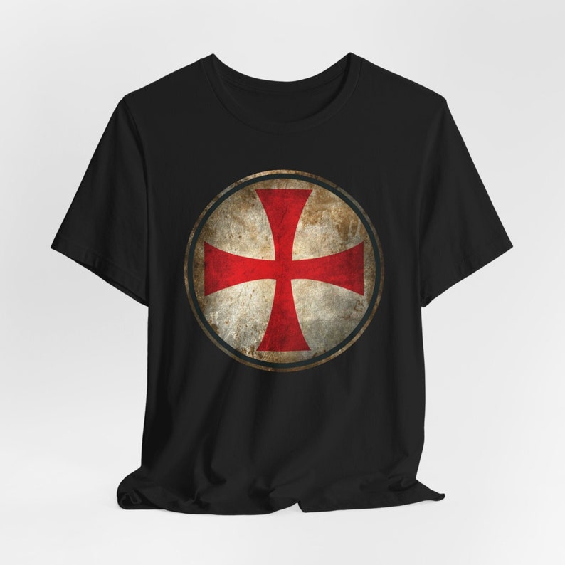 May include: Black t-shirt with a red cross in a circle on the front. The cross is on a white background with a distressed, vintage look.