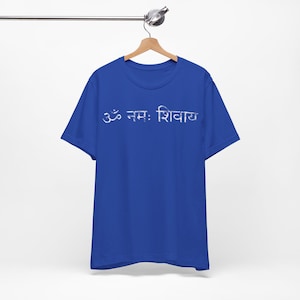 May include: A royal blue short-sleeved t-shirt featuring the white Devanagari script text Om Namah Shivaya printed across the chest. The garment has a crew neckline and is displayed on a wooden hanger against a plain white background.