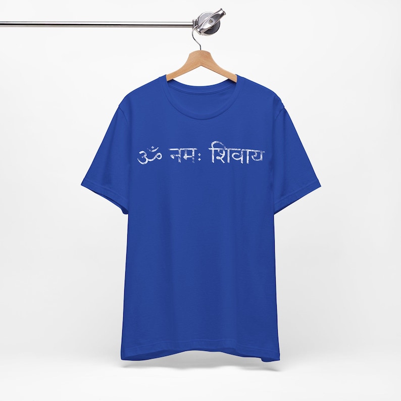 May include: A royal blue short-sleeved t-shirt featuring the white Devanagari script text Om Namah Shivaya printed across the chest. The garment has a crew neckline and is displayed on a wooden hanger against a plain white background.