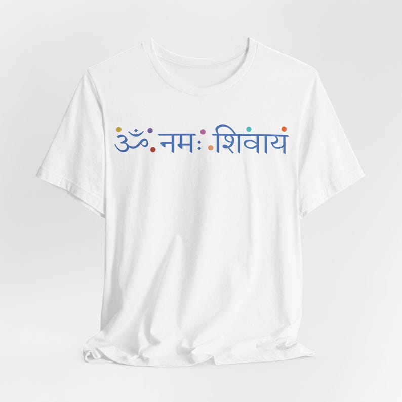 May include: A white short-sleeved t-shirt featuring the blue Sanskrit text Om Namah Shivaya printed across the chest. The design includes small, colourful circular dots interspersed between the characters of the script in a horizontal line.