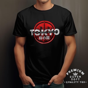 Può includere: T-shirt nero con un design grafico rosso e bianco. Il design include la parola "TOKYO" in bianco, un cerchio rosso con una silhouette di paesaggio urbano e testo giapponese. La maglietta ha anche il testo "LAND OF CHERRY BLOSSOMS".
