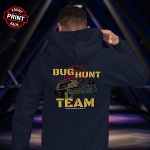 Può includere: Felpa con cappuccio blu navy con grafica "BUG HUNT TEAM" gialla e rossa sul retro, raffigurante un'arma stilizzata. Sul davanti è presente un timbro circolare rosso e bianco con la scritta "FRONT PRINT BACK".