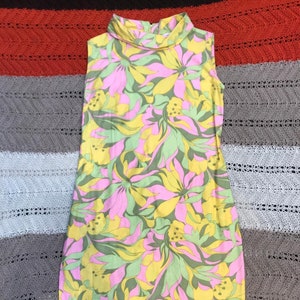 K&ouml;nnte beinhalten: Ein &auml;rmelloses Kleid mit hohem Kragen und einem Blumendruck in Rosa-, Gelb- und Gr&uuml;nt&ouml;nen.
