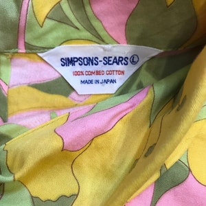 K&ouml;nnte beinhalten: Ein Hemd mit gelbem, rosa und gr&uuml;nem Blumendruck und einem wei&szlig;en Etikett mit der Aufschrift "SIMPSONS-SEARS&reg; 100% GEK&Auml;MMTE BAUMWOLLE HERGESTELLT IN JAPAN".