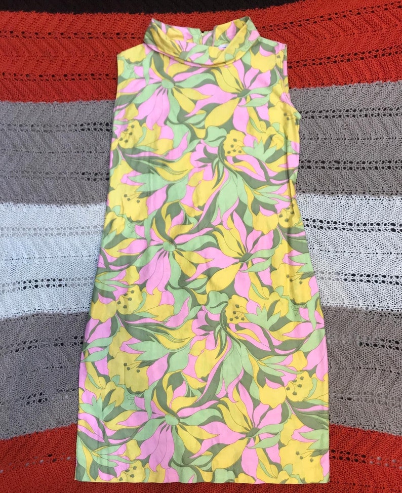 K&ouml;nnte beinhalten: Ein &auml;rmelloses Kleid mit hohem Kragen und einem Blumendruck in Rosa-, Gelb- und Gr&uuml;nt&ouml;nen.