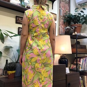 K&ouml;nnte beinhalten: Ein &auml;rmelloses Kleid mit einem pinkfarbenen, gelben und gr&uuml;nen Blumendruck. Das Kleid hat einen Kragen und einen Knopfverschluss auf der R&uuml;ckseite.
