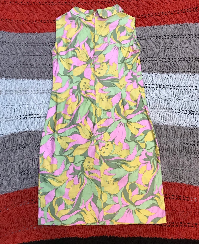 K&ouml;nnte beinhalten: Ein &auml;rmelloses Kleid mit einem pinkfarbenen, gelben und gr&uuml;nen Blumendruck. Das Kleid hat einen Kragen und einen Rei&szlig;verschluss auf der R&uuml;ckseite.