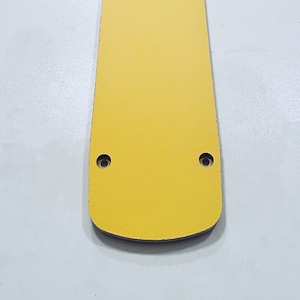 May include: A yellow rectangular plate with rounded edges and four evenly spaced holes. The plate is made of a smooth, hard material.