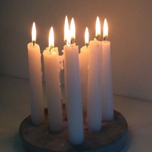 Può includere: Un set di sette candele bianche disposte in un cerchio su una base di cemento grigia. Le candele sono accese e proiettano un bagliore caldo.