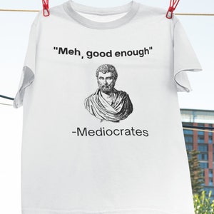 May include: White t-shirt with a black and white illustration of a man's bust and the text "Meh, good enough" and "-Mediocrates".
