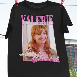 Op de afbeelding: Zwart T-shirt met een roze afbeelding van een vrouw met rood haar en de tekst "Valerie Cherish".