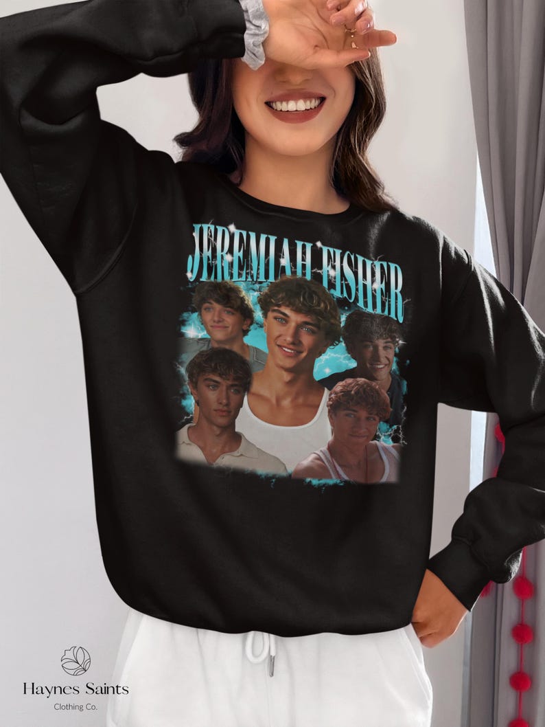 May include: Black sweatshirt featuring a graphic of the name "Jeremiah Fisher" in turquoise lettering, with multiple images of a young man. The sweatshirt has a crew neck and long sleeves. The brand name "Haynes Saints Clothing Co." is printed at the bottom.