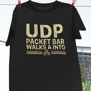 Könnte beinhalten: Schwarzes T-Shirt mit einem Grafikdruck im Vintage-Stil, der "UDP Packet Bar Walks A Into" mit einem pixeligen Design zeigt.