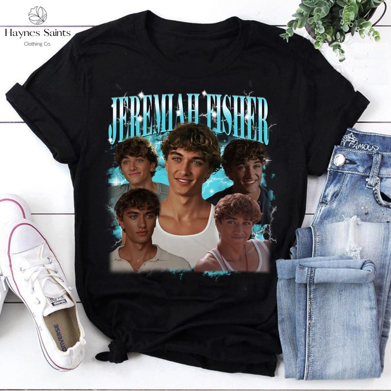 May include: Black t-shirt featuring a graphic of the name "Jeremiah Fisher" in a light blue font, with multiple images of a young man. The shirt is paired with blue jeans and white sneakers.