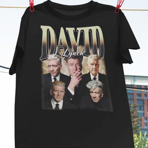 Puede incluir: Camiseta negra con un estampado gráfico de David Lynch y el texto "DAVID Lynch" en estilo vintage.