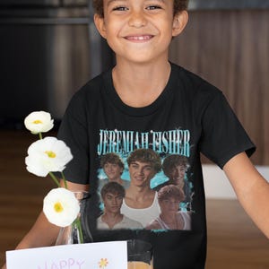 May include: A young person wearing a black t-shirt with the text "JEREMIAH FISHER" above a photo collage of young men. The image also includes a "Happy Mother's Day" card, strawberries, and a plate of eggs and toast.