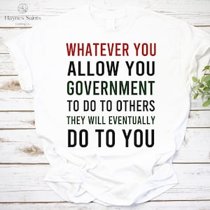 Pode incluir: Camiseta branca com o texto "WHATEVER YOU ALLOW YOU GOVERNMENT TO DO TO OTHERS THEY WILL EVENTUALLY DO TO YOU" em vermelho, preto e verde. A camiseta tem o logotipo "Haynes Saints Clothing Co.".