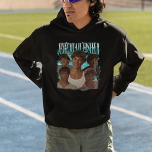 May include: Black hooded sweatshirt featuring the text "JEREMIAH FISHER" above a collage of images. The sweatshirt is worn by a person wearing sunglasses. The brand logo "Haynes Saints Clothing Co." is visible at the bottom.