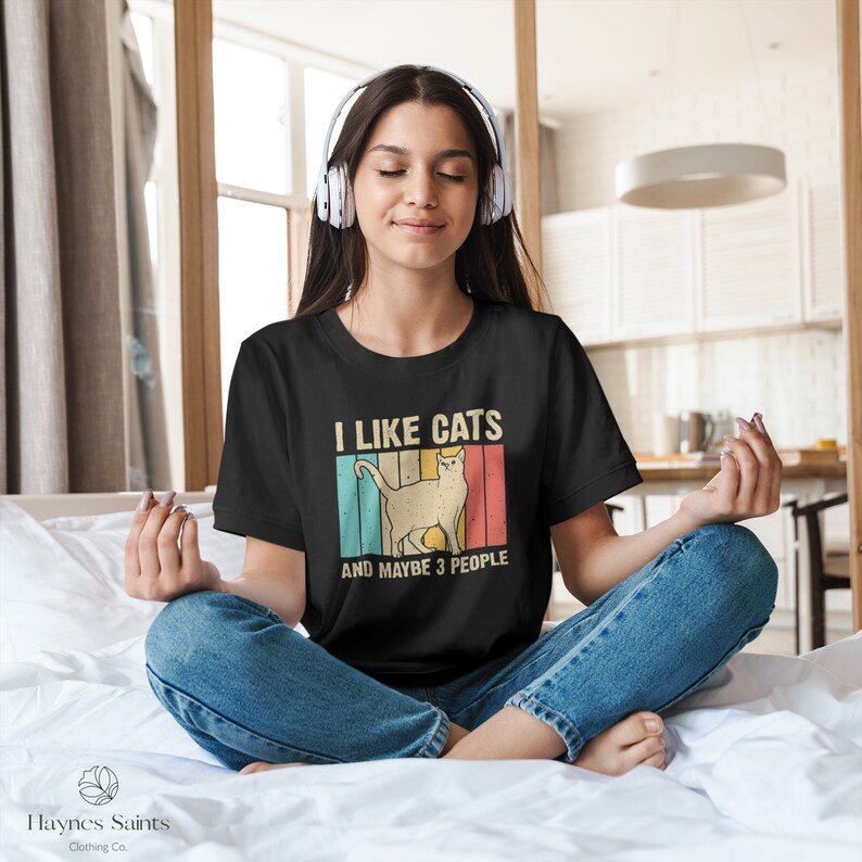 May include: A person wearing a black t-shirt with a vintage-style graphic that says "I like cats and maybe 3 people". The graphic features a white cat with a retro color scheme.