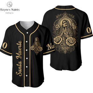 Op de afbeelding: Zwart honkbalshirt met gouden rand en accenten. De voorkant heeft de tekst "Santa Muerte" en een afbeelding van een skeletheilige. De achterkant toont een groter skeletheilige-ontwerp met rozen. Het shirt heeft het nummer "0" op de mouwen.