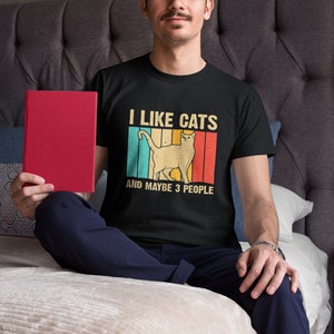 May include: A black t-shirt with a vintage-style graphic of a cat and the text "I like cats and maybe 3 people".