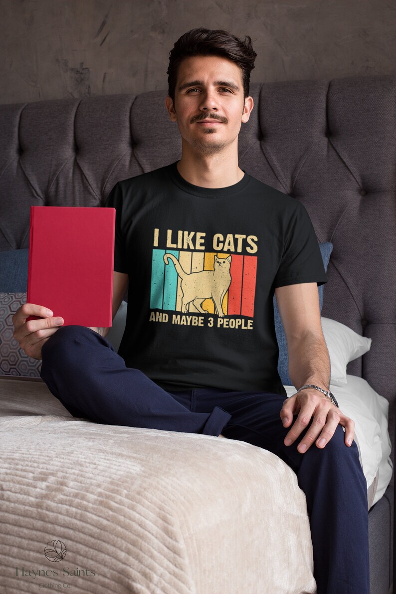 May include: A black t-shirt with a vintage-style graphic of a cat and the text "I like cats and maybe 3 people".