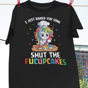 May include: Black t-shirt featuring a rainbow unicorn wearing a chef's hat and frosting cupcakes. The text reads "I just baked you some shut the fucupcakes".