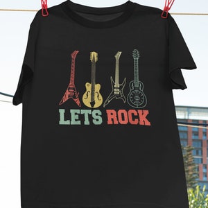 Op de afbeelding: Zwart T-shirt met een vintage-stijl grafische afbeelding van vijf verschillende gitaren en de tekst "LETS ROCK".