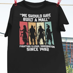 Op de afbeelding: Zwart T-shirt met een vintage-stijl grafische afbeelding van Amerikaanse indianen. De tekst luidt "We should have built a wall" en "Fighting illegal immigration since 1492".